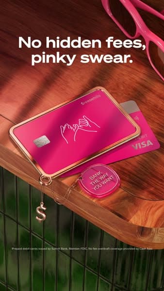 A pink Cash App Visa card and matching keychain rest on a wooden surface next to pink glasses, with the headline text "No hidden fees, pinky swear." visible above them.