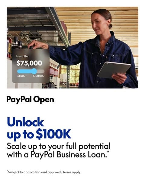 A woman in a blue jacket holding a tablet selects a $75,000 loan offer on a digital slider overlay in a store, with text below reading "PayPal Open Unlock up to $100K Scale up to your full potential with a PayPal Business Loan.*" and fine print "*Subject to application and approval. Terms apply.