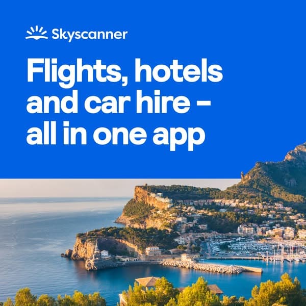 Advertising banner with a blue upper half and a scenic coastal town view below, featuring the Skyscanner logo and the headline text "Flights, hotels and car hire – all in one app.